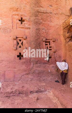 Pellegrino che prega al muro della chiesa di Bete Medhane Alem in Lalibela Etiopia Foto Stock