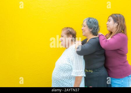 Profili di vista laterale di nonna, figlia e nipote che riposano sulle loro spalle, tre generazioni di donne messicane sorridenti con stoffa casual Foto Stock