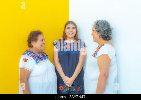 Tre generazioni di donne messicane sorridenti con stampe floreali bluse, madre e figlia che si guardano l'un l'altro e la nipote nel mezzo di Foto Stock