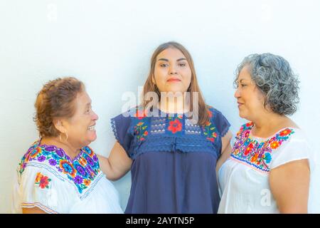 Madre e figlia che si guardano l'un l'altro e nipote nel mezzo di loro, tre generazioni di donne messicane sorridenti con stampa floreale blous Foto Stock