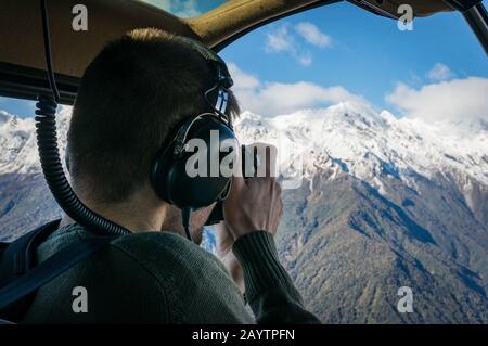 Unrecognizable persona che scatta foto aeree di montagne di neve da elicottero, aereo Foto Stock