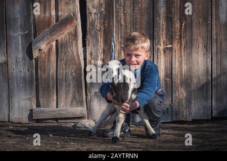 Villaggio di Krastava, montagne di Rhodope / Bulgaria : Ritratto di piccolo ragazzo abbraccio agnello nella fattoria. Foto Stock