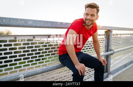 L'uomo runner prendendo una pausa durante il corso di formazione all'esterno. Appoggio del pareggiatore dopo l'esecuzione. Foto Stock