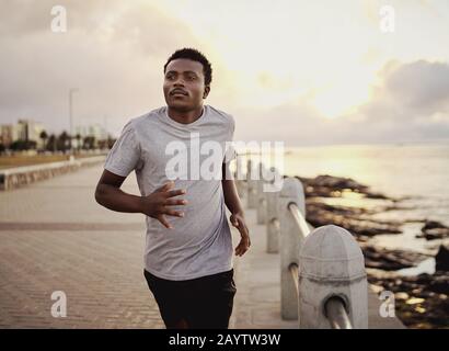 Un giovane atleta sicuro che corre sul lungomare durante la mattina presto Foto Stock