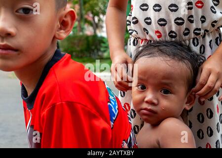 Due bambini accompagnano un bambino senzatetto mentre si siedono su un trattore giocattolo su una strada della città nella città Kampong Cham, Cambogia. Foto Stock