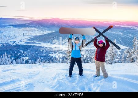 Amici snowboarder e sciatore in piedi sulla cima della montagna cielo blu alba. Concept stazione sciistica foresta invernale Foto Stock