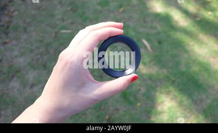 Una mano che tiene una lente ravvicinata, con prato verde sullo sfondo. Foto Stock