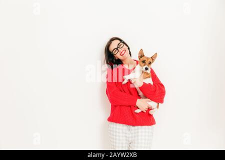 Foto di lieti caucasico porta femmina jack russell terrier cane, indossa gli occhiali e maglione rosso, gode di tempo libero con animale preferito, pongono aga Foto Stock