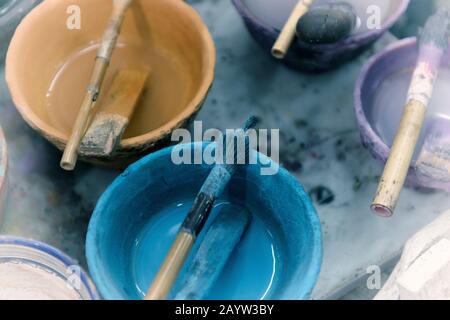 Dipingere in ciotole con semplici pennelli in uno studio d'artista. Immagine di sfondo vintage con venatura della pellicola. Foto Stock