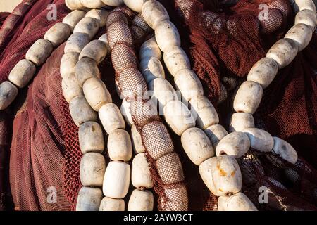 Colore Bordeaux delle reti da pesca, con linee bianche delle boe. Palo illuminato dalla luce del sole del mattino. Porto Di Essaouira, Marocco. Foto Stock