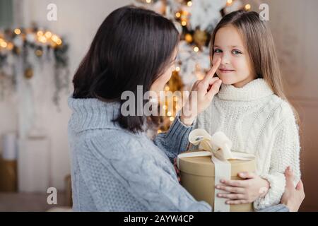 Ritratto di adorabili poco kid e madre, tocca il suo piccolo naso, dà avvolto confezione regalo, prepara poco surpise per la figlia, dà presente nelle vicinanze Foto Stock