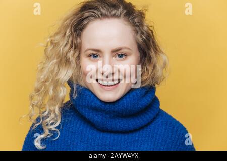 Felice felice felice donna con capelli chiari croccanti, indossa caldo maglione blu, ha un ampio sorriso e denti bianchi essere soddisfatti dopo il successo giorno, isolato o Foto Stock