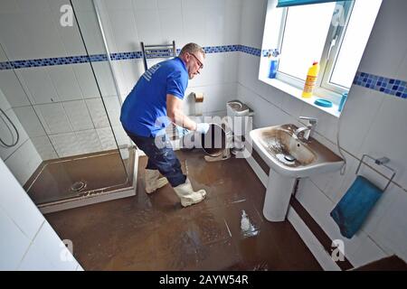 Peter Maybury, un esperto di pulizia tappeti e tappezzeria, la rimozione di  un bidone da un bagno allagato in una proprietà di Oxford Street, Nantgarw,  nel Galles del Sud, dove i residenti