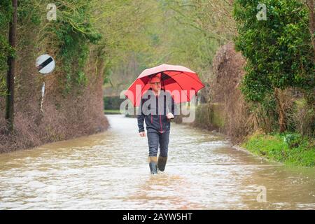 L'uomo cammina lungo una strada allagata che tiene un ombrello, durante la tempesta Dennis. Molto Hadham, Hertfordshire. REGNO UNITO Foto Stock