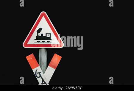 Segno di attraversamento del treno e un crossbuck bianco rosso di fronte a un binario ferroviario. Segnale di avvertimento isolato su sfondo nero Foto Stock