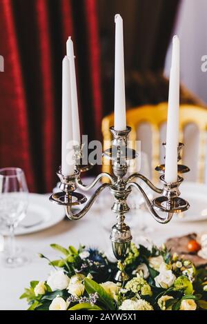 Lussuoso tavolo da banchetto servito con un bel candelabro con candele bianche, fiori, tovaglie e piatti. Ristorante in stile retrò. E meraviglioso Foto Stock