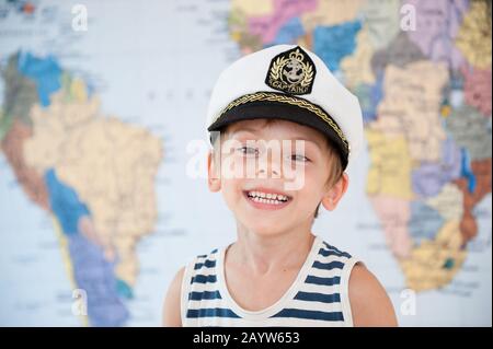 giro del mondo crociera concetto di felice sorridente bambino piccolo in cappello capitano su sfondo geografico mappa