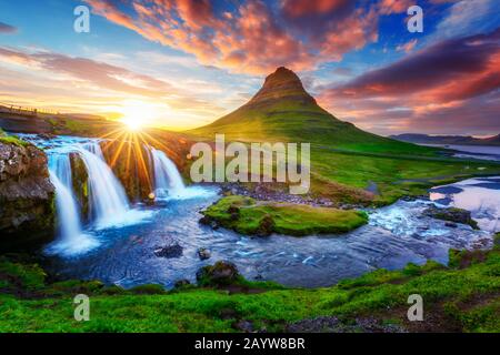 Splendido paesaggio con il sole che sorge sulla cascata Kirkjufellsfoss e sulla montagna Kirkjufell, Islanda, Europa. Foto Stock