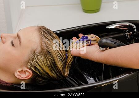 Stylist per capelli applicazione di shampoo colorito viola dopo la tintura dei capelli. Foto Stock