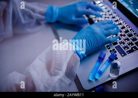 La provetta per analisi del sangue per il mantenimento del personale infermieristico è in tuta protettiva bianca per il Hazmat in un computer da laboratorio. Studio concettuale antidoto contro l'epidemia Foto Stock