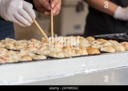 Mani che usano i bastoni per girare takoyaki mentre lo cucinano. Takoyaki è un alimento giapponese popolare conosciuto con il relativo ingrediente principale - polpo. Foto Stock