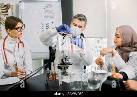 Team di scienziati professionisti, operatori di laboratorio in uniforme analisi di nuove sostanze, analisi di campioni di sangue o nuovi farmaci. Provetta di riempimento per medico maschio Foto Stock