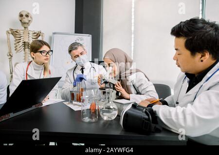 scienza, chimica, microbiologia, medicina. Scienziati multietnici che lavorano con microscopi, matracci e provette che effettuano test o ricerche Foto Stock