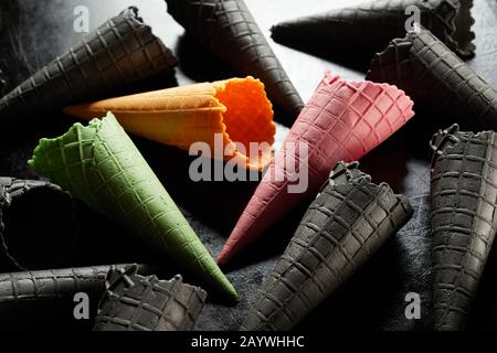 Colori assortiti di coni gelato a cialda con singoli rosa, verdi e gialli tra una selezione di neri su un backgroun grigio monocromatico Foto Stock