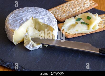 Formaggio Camembert essendo spalmato su cracker sul formaggio scheda di ardesia Foto Stock