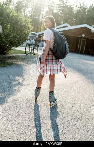 Donna caucasica con zaino urbano pattinaggio a rotelle in una soleggiata giornata estiva. Vacanze attive. Foto Stock