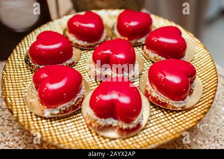 candy bar. Torta mousse alla moda in forma di cuore con specchio rosso glassa e scaglie di cocco su piastra d'oro. Dessert moderno. San Valentino Foto Stock