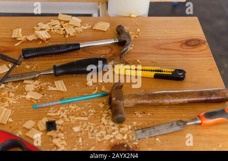 Martelli, scalpello, taglierino, matita tenuto su un tavolo disordinato riempito con trucioli di legno di scarto. Alcuni attrezzi usati dell'officina di lavorazione del legno. Foto Stock