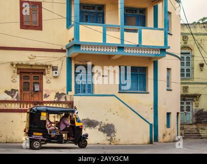 Un quartiere tranquillo di vecchi edifici residenziali con finestre blu e marrone a Diu. Una corsa in risciò sulla strada. Foto Stock
