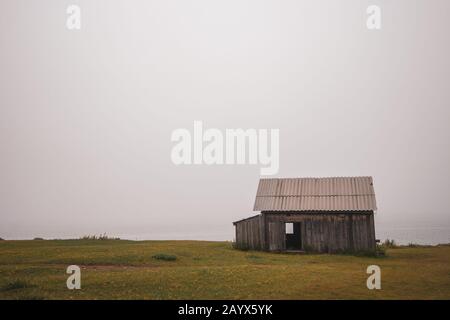 Casa solitaria nella nebbia sulla riva del lago Baikal. Capannone con porte aperte. Erba verde. Tempo nuvoloso. Foto Stock