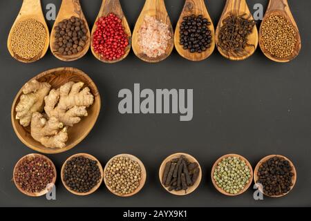 Sette cucchiai da cucina in legno d'oliva in fila e sei piccole ciotole in legno in fila piene di varie spezie e una ciotola in legno con radici di zenzero Foto Stock