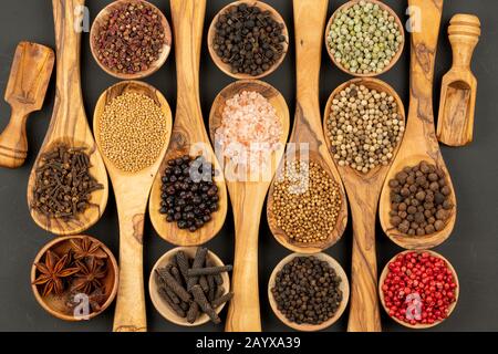 Spezie e cibo - sfondo fatto di molte varietà di spezie e pepe in piccole ciotole di legno e cucchiai di cottura in legno di oliva su una ba nera Foto Stock