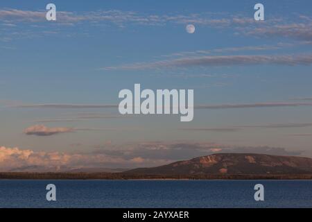 La luna piena in un cielo blu crepuscolo che riflette il sole che tramonta sopra il Parco Nazionale di Yellowstone, Wyoming. Foto Stock