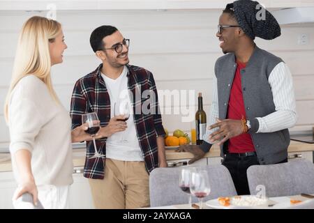 Gruppo di giovani amici bere vino e ascoltare il ragazzo afro-americano a casa festa Foto Stock