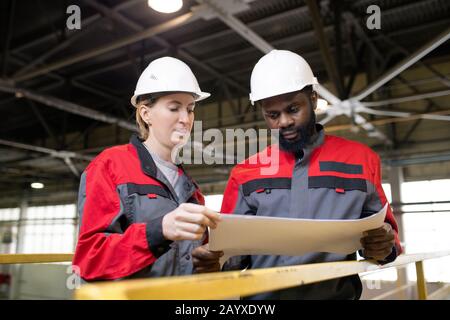 Ritratto orizzontale a basso angolo di due tecnici di fabbrica professionisti che lavorano insieme su un nuovo progetto Foto Stock