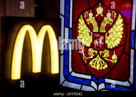 Mosca, Russia. 14th di Febbraio, 2020 McDonald's catena di ristoranti logo sullo sfondo dello stemma della Federazione Russa nella costruzione del negozio Detsky Mir (Children's World) sulla via Lubyanka a Mosca, Russia Foto Stock