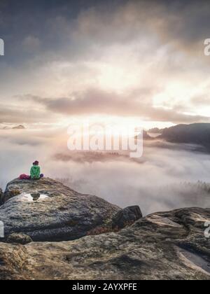 Viaggiare da soli donna escursionista si siede sul bordo della scogliera e godendovi l'alba guardando la valle e le montagne. Viaggiando uno stile di vita attivo concept Foto Stock