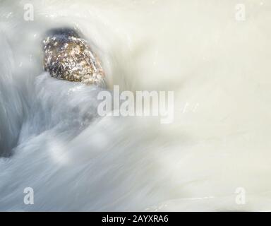 Il fiume bianco di montagna di Milky scorre oltre una pietra Foto Stock