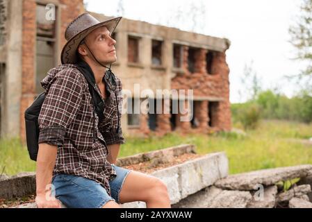 Un uomo in un cappello da cowboy si siede in mezzo a una casa rovinata. Foto Stock