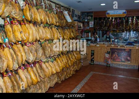 Il prosciutto andaluso essiccato all'aria è appeso in un negozio di specialità nella città storica di Ronda nella provincia spagnola di Malaga in Andalusia, Spagna. Foto Stock