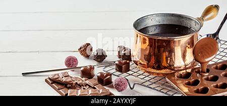 Preparazione di cioccolatini di lusso fatti a mano Valentines che versano il cioccolato fuso da una pentola di rame in uno stampo con bononi assortiti su una rastrelliera metallica Foto Stock