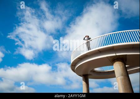 Uomo d'affari lontano in piedi all'aperto su un passaggio curvo che guarda fuori in cielo blu brillante Foto Stock