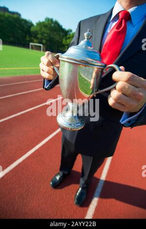 Irriconoscibile imprenditore tenendo in mano un trofeo di argento all'aperto nella parte anteriore del rosso acceso via Foto Stock