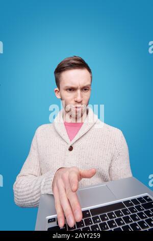 Scioccato giovane uomo barbuto in cardigan utilizzando un moderno notebook su sfondo blu Foto Stock