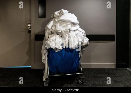 Trolley pieno di lenzuola bianche sporche di ospiti in un hotel. Foto Stock