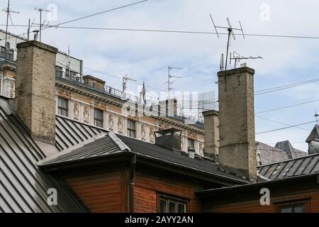 Edificio Art Nouveau accanto ad una vecchia casa in legno con molte antenne tv e camini sul tetto Foto Stock